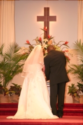 A couple are married under a cross and surrounded by plants and flowers in a church