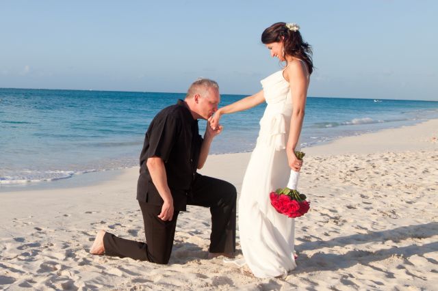 A man kneels and kisses the hand of a beautiful woman at the beach