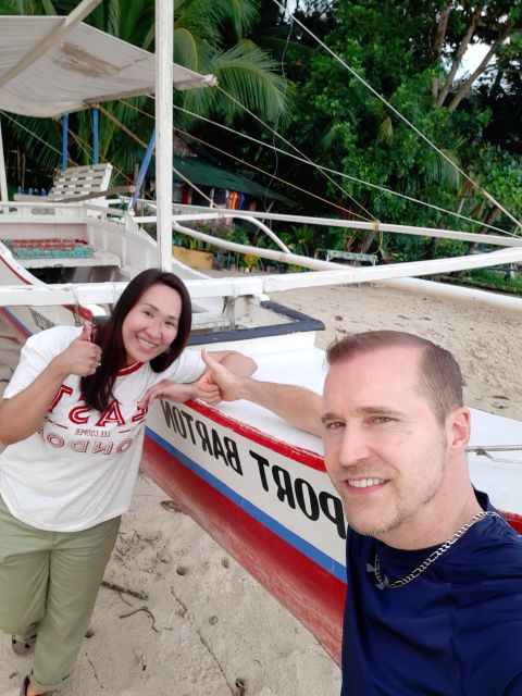 Wife gives thumbs up sign while holding husbands hand next to boat