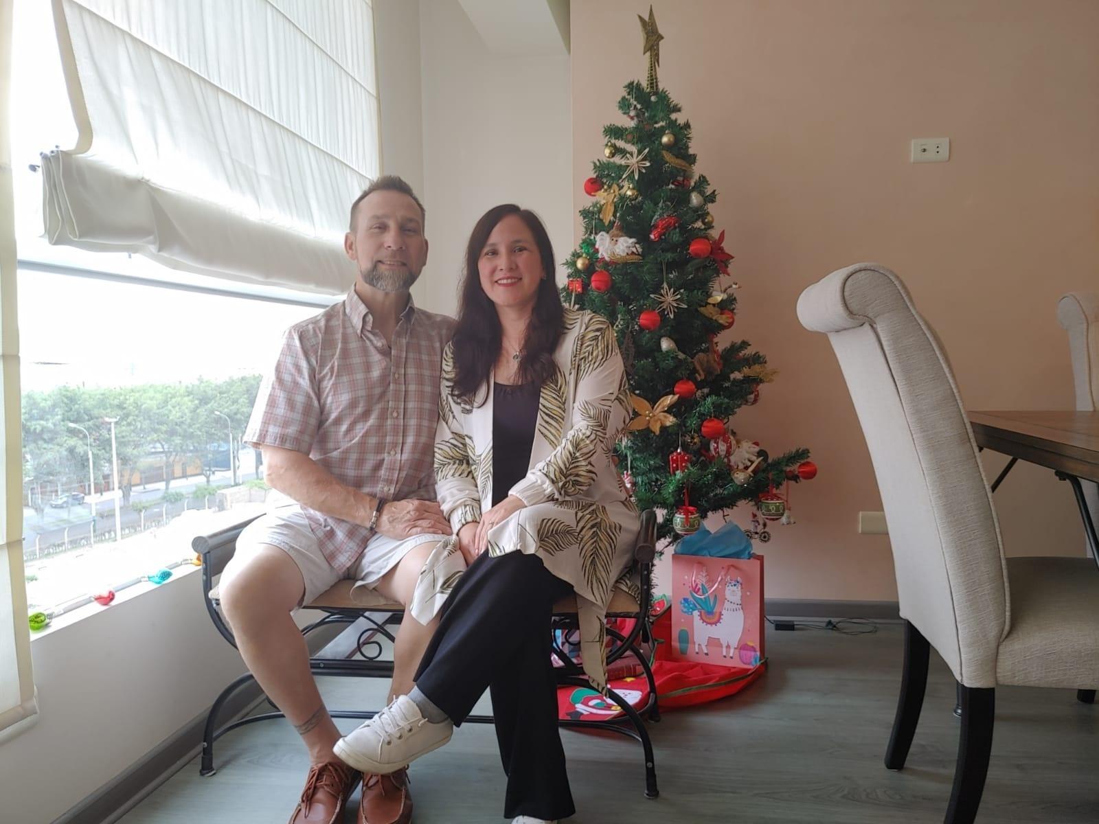 A mixed Christian couple hold hands while sitting in front of a Christmas tree