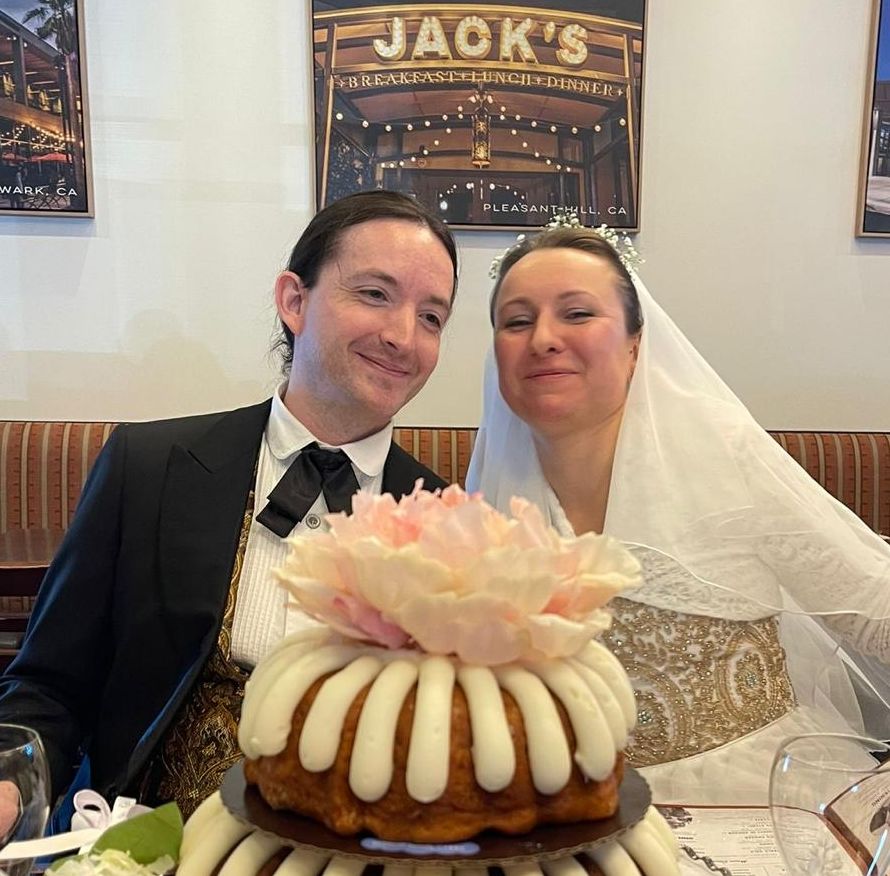 A beautiful Christian bride and husband smile while seated behind a uniquely decorated wedding cake
