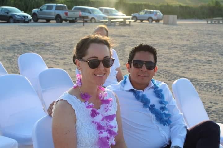 Christian singles sit side by side in chairs at a beach wedding, while wearing Hawaiian leis