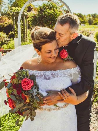 Tender kiss and embrace from Happily married groom who hugs his bride in wedding dress with rose bouquet