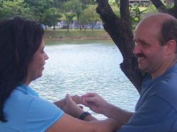 A very happy man puts an engagement ring on a woman while standing near a beach