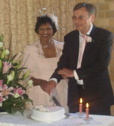 Man pulls his hand away from flame as he cuts wedding cake next to his smiling wife