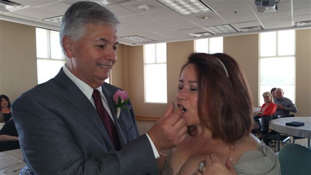 Man smiles while tries feeding his wife some wedding cake