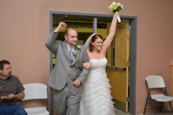 A triumphant bride and groom storm into a reception room smiling
