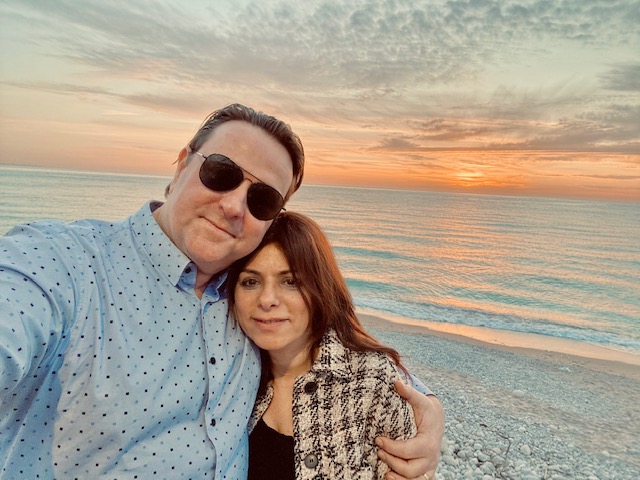 A couple enjoys a selfie on the beach at sunset while the waves roll in