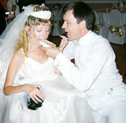 Newlyweds laugh as they try to feed each other wedding cake