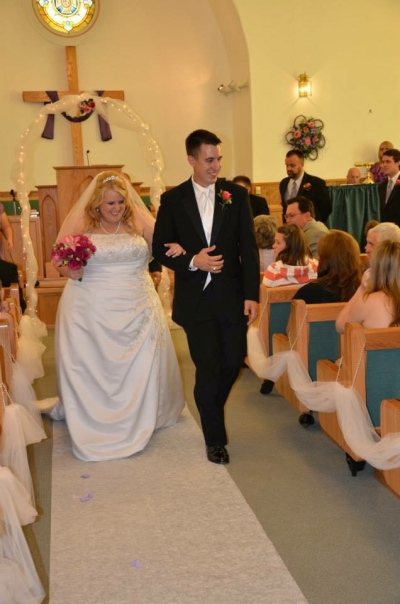 Walking down the aisle, bride in white dress and red bouquet holding arm of husband in black suit