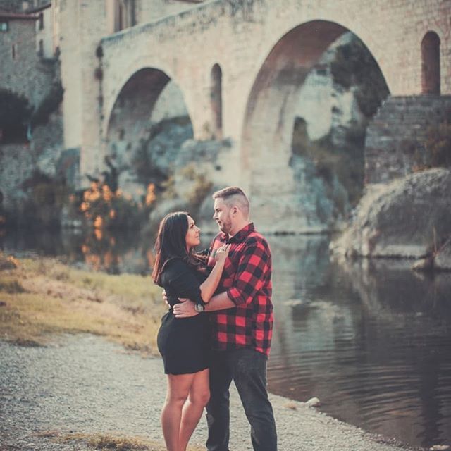 Christian woman in black dress in tender embrace from husband with Bridge in background