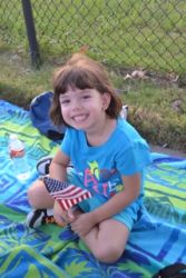 A contented girl sits in a park holding an American flag