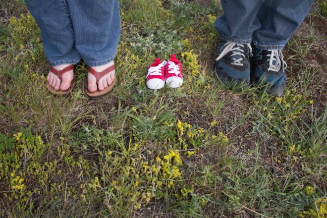 A man and a woman stand on grass in shoes with infant shoes between them