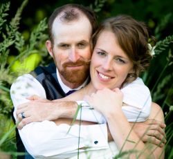 A confident looking man has his arms draped around a beautiful woman who smiles lovingly