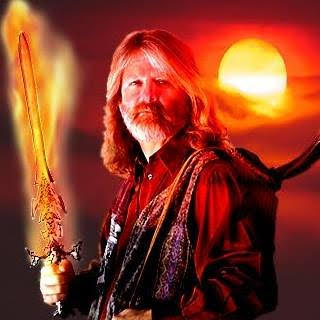 A man with a beard and flowing hair holds a flaming sword as the sun sets behind him