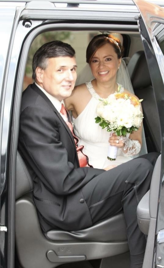 Formerly divorced Christian man is seated in a car beaming with joy as his beautiful new bride smiles from inside the car